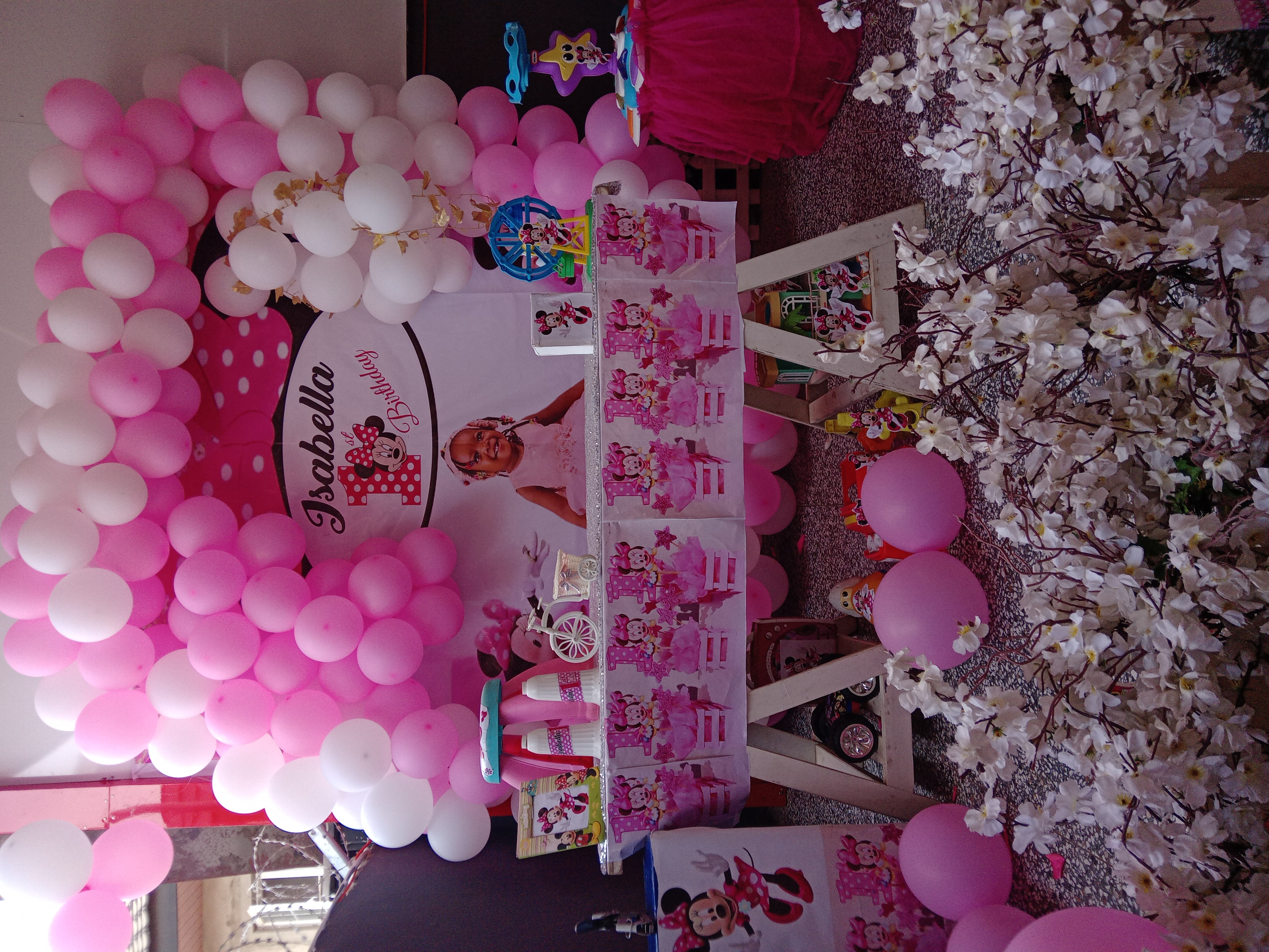 Minnie Mouse first birthday backdrop with pink and white balloons and a styled gift table