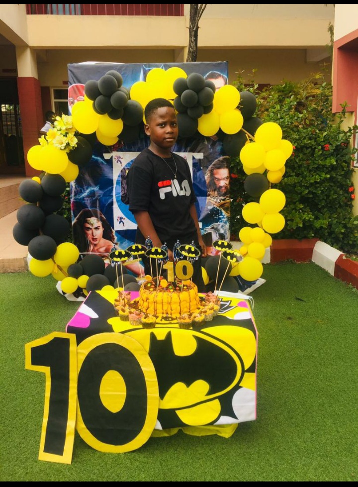 Birthday child at a Batman-themed cake table with black and yellow balloons