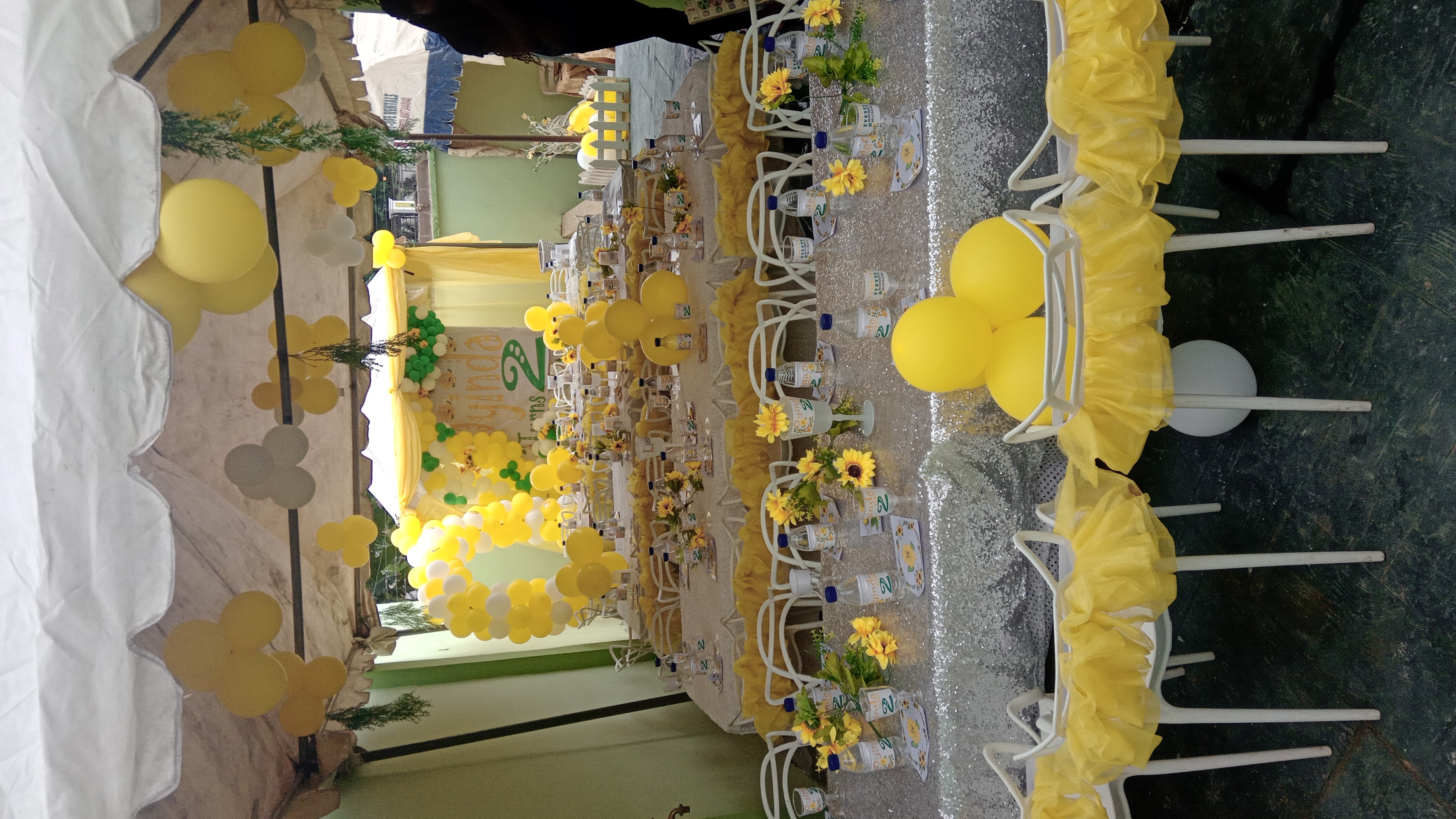 Yellow and white birthday party tables with flowers and balloon decorations