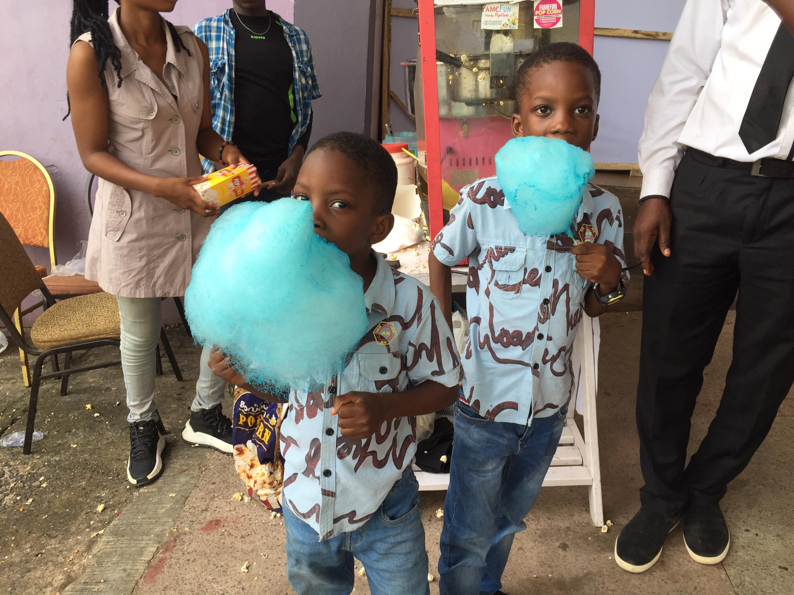 Two children holding blue cotton candy beside a Fame Fun popcorn machine